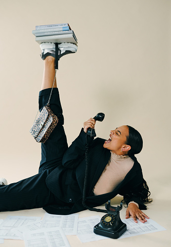 Studio shot of a beautiful young woman balancing a pile of books on her foot while screaming into a telephone against a brown background