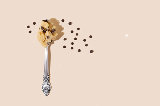 Edible cookie dough in spoon with chocolate chips on the yellow background in sunlight, close up.