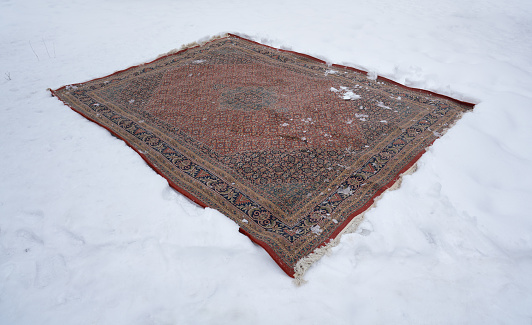 Old Persian rug upside down in the snow as a way to clean it