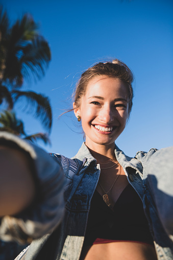 Personal perspective viewpoint of a young woman taking a selfie in warm sunlight, palm trees in the background, in Fort Lauderdale, Florida.