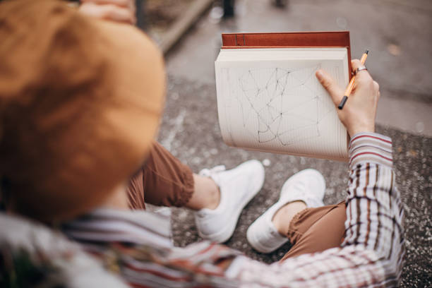 One man, young male artist sitting on steps outdoors in city, he is drawing in his notebook.