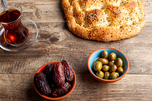 Angled view of the traditional meal for iftar and sahur in the holly month of Ramadan. Turkish tea in special glasses, ramazan pidesi,  a type of flatbread, date fruit and olives in oil.