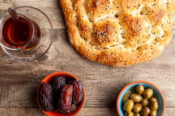 Flat lay image of a traditional meal for iftar and sahur in the holly fasting month of Ramadan. Turkish tea in special glasses, ramazan pidesi,  a type of flatbread, date fruit and olives in oil.