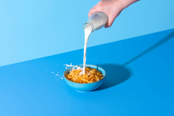 verser le lait dans un bol de céréales sur un fond bleu. cornflakes et lait. - céréales du petit déjeuner photos et images de collection