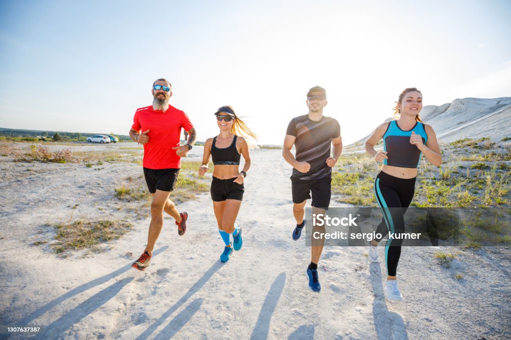 Four friends run together on trail running Group of four friends run together on trail running. Wide angle view with long shadows 20-29 Years Stock Photo