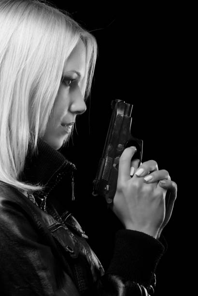 Young blonde woman shooting a handgun isolated on black background.
