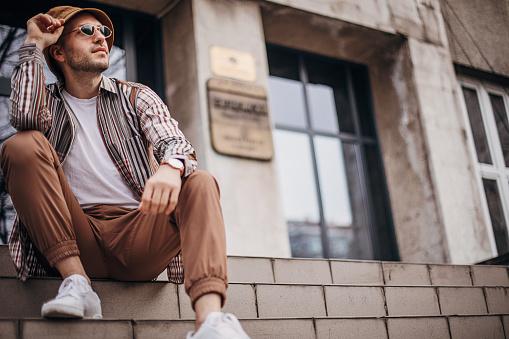 One man, young modern fashionable man, sitting on steps outdoors in city.