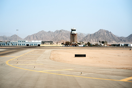 Dry yellow sand of desert and blue sky. Airport runway foreground. Air traffic control tower in airport, Egypt