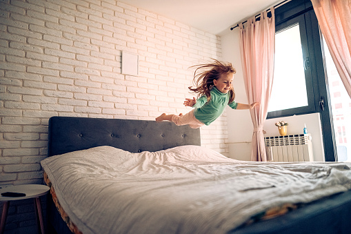 Girl playing in bedroom, jumping on bed
