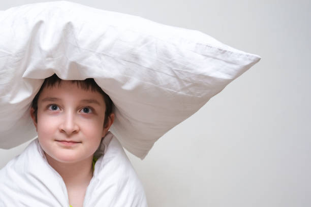 istock A thoughtful boy in blanket with a pillow on the head, sleeping dreaming concept, copy space, white background 1307641595