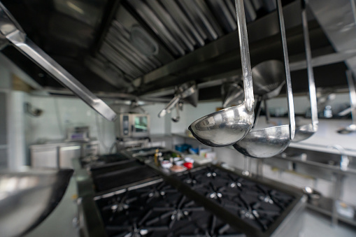 Commercial kitchen at a restaurant or gastronomy school - focus on cooking utensils hanging from the top