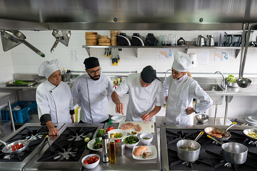 Group of Latin American cooks cooking together in the kitchen at a restaurant and paying attention to the chef