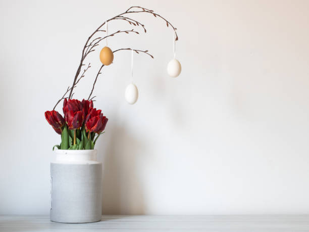 istock Interior photography concept Easter. On a solid background, a vase with red tulips and a branch on which eggs hang. There is a place for the text 1307643682