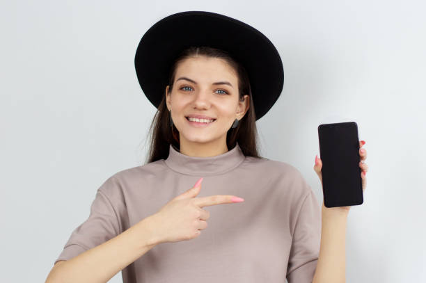 istock Smiling woman is pointing on smartphone standing on white background. 1307644783