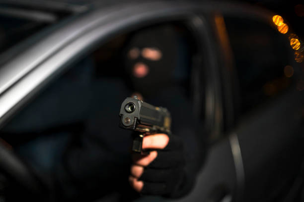 Masked man with handgun driving a car Man in black balaclava with handgun driving a car. Car thief, car theft man holding gun at night in the city stock pictures, royalty-free photos & images