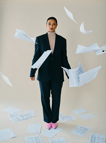 Studio portrait of a beautiful young woman surrounded by paperwork falling around her against a brown background