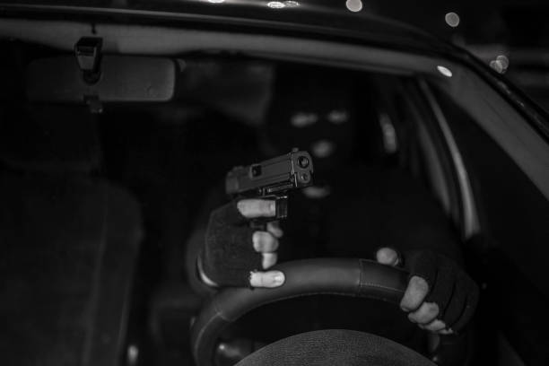 Masked man with handgun driving a car Man in black balaclava with handgun driving a car. Car thief, car theft man holding gun at night in the city stock pictures, royalty-free photos & images