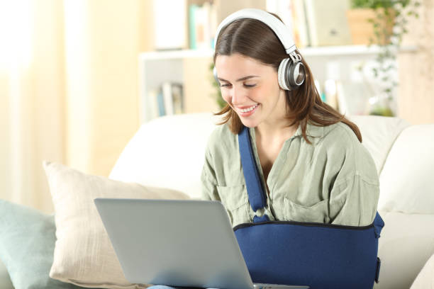 feliz mujer discapacitada usando computadora portátil y auriculares - arm sling fotografías e imágenes de stock