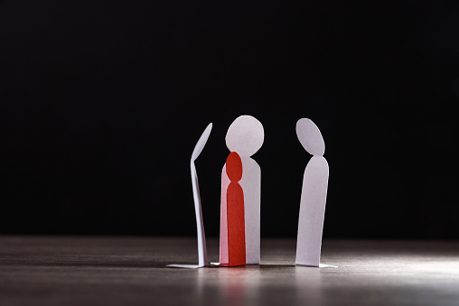 Child bullying concept with cutouts of little paper men on wooden table and dark background