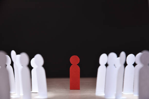 Social discrimination many paper men front dark social discrimination concept with many little white paper men around a different one on wooden base and dark background front view prejudice stock pictures, royalty-free photos & images