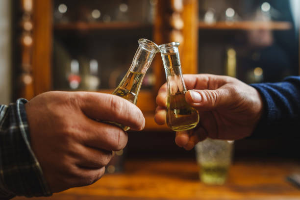 Close up on hands of two unknown men toasting with traditional serbian drink plum brandy rakija slivovitza holding glass called cokance at home stock photo