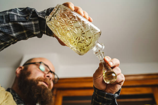 side view of adult caucasian bold man with beard pouring traditional serbian bosnian croatian or macedonian drink alcohol brandy rakija or slivovitza made from plum in special glass cokance at home - slivovitz imagens e fotografias de stock