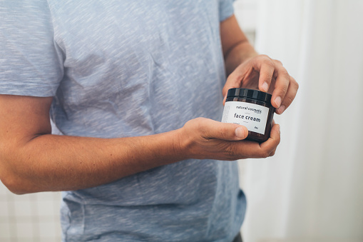 Close up shot of an anonymous young Caucasian man opening a face cream jar after a morning shave in a bathroom.