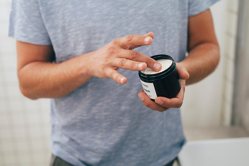 Close up shot of an anonymous young Caucasian man opening an aftershave moisturizer after a morning shave in a bathroom.