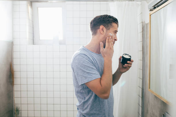 Handsome happy young Caucasian man applying face cream after a morning shave.