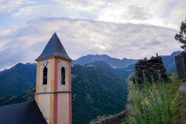 campanario de la iglesia de la localidad pirenaica catalana de canejan, con colores crema, rojo y amarillo y las montañas al fondo - pyrenean fotografías e imágenes de stock