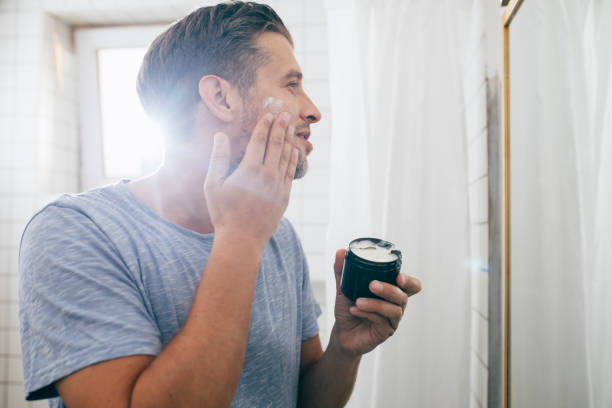 Handsome Young Man Applying Face Cream after a Morning Shave Handsome happy young Caucasian man applying face cream after a morning shave. face cream stock pictures, royalty-free photos & images