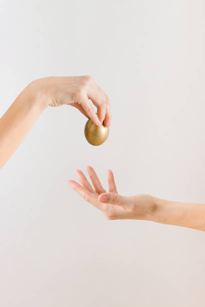 istock Beautiful woman's hands with golden Easter egg on the pastel beige background with a copy space. Minimalist giving Easter eggs idea. Art concept. 1307656568