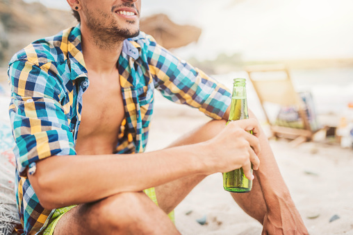 Young man with sun tan holding beer at the beach. Summer vacation concept.