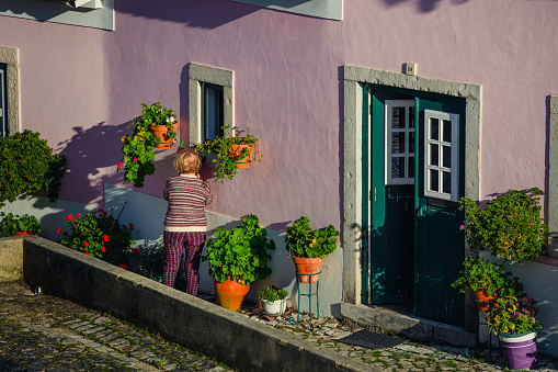 Óbidos, Portugal - December 10, 2018: an old woman watering plants outside her house in the city of Óbidos, in the Leiria District of Portugal.
