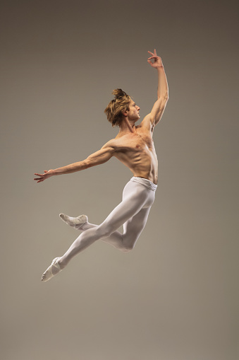 Muscular. Young and graceful ballet dancer isolated on studio background in flight, jump. Art, motion, action, flexibility, inspiration concept. Flexible caucasian ballet dancer, moves in glow.