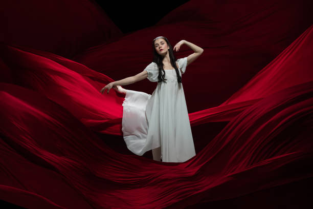 istock Young and graceful ballet dancer on billowing red cloth background in classic action. Art, motion, action, flexibility, inspiration concept. 1307664192