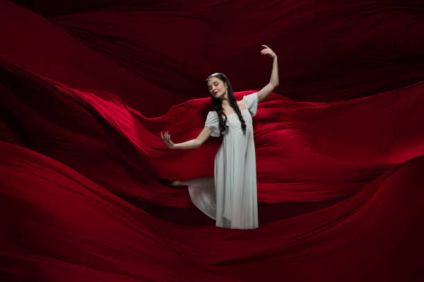 istock Young and graceful ballet dancer on billowing red cloth background in classic action. Art, motion, action, flexibility, inspiration concept. 1307664198