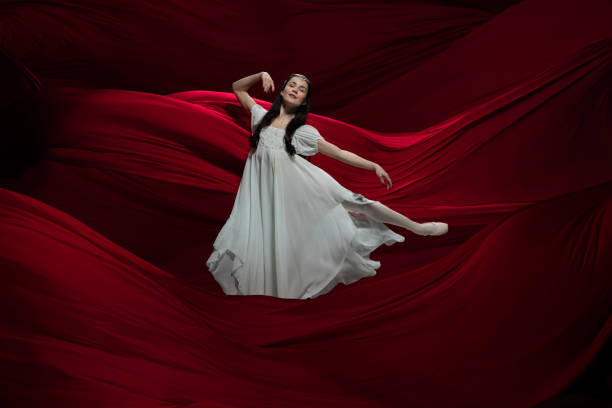 istock Young and graceful ballet dancer on billowing red cloth background in classic action. Art, motion, action, flexibility, inspiration concept. 1307664199