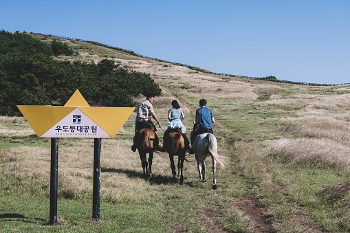 Udo, Jeju Island, South Korea - September 13, 2019: A guide leads two tourists on a horseback ride near the lighthouse on Udo, a small island located off the coast of Jeju island.