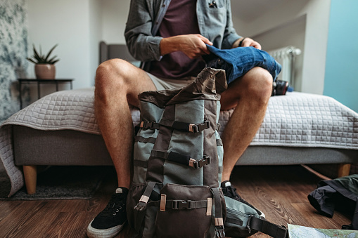 Young man packing backpack to visit city, preparing in his hotel room
