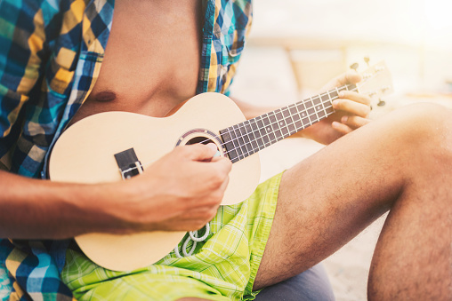 Young man playing a ukulele guitar at the beach. Summer vacation / Arts concept.