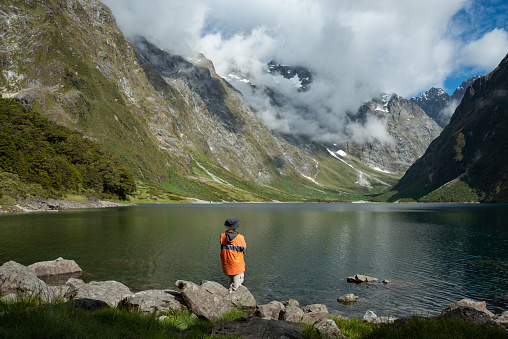 A tourist standing on the shore of Lake Marian and enjoying the views, Fiordland National Park, New Zealand.