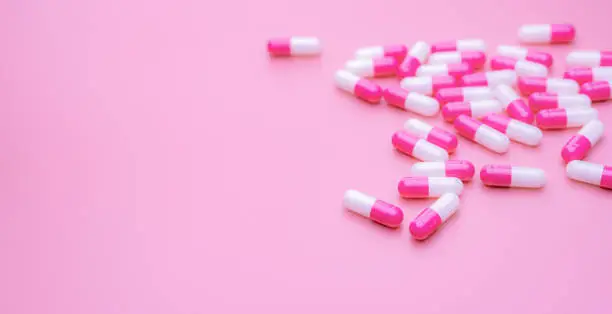 Pink-white antibiotic capsules pill spread on pink background with space. Pharmacy banner. Antibiotic capsule pills. Pharmacy shop wallpaper. Pharmaceutical industry. Antimicrobial drugs. Healthcare.