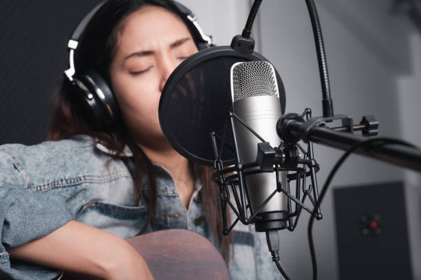 istock Asian female singer with a passion for music and microphone. While playing her guitar in a professional studio. Music concept, sound recording concept. 1307690747