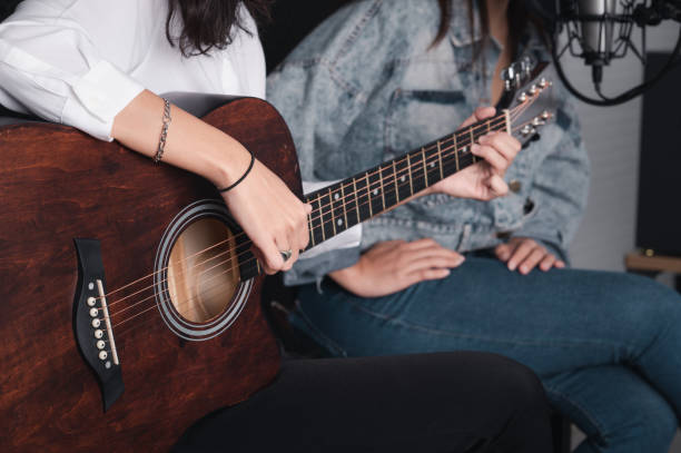 istock Asian female singer with a passion for music and microphone. While playing her guitar in a professional studio. Music concept, sound recording concept. 1307690773