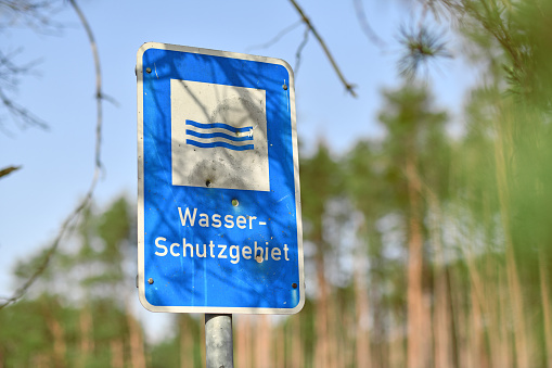 Blue sign with German text 'Water protection area' with bullet holes with blurry forest background