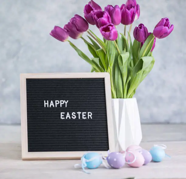 Spring concept. Bouquet of purple tulips flowers and letter board with the words Happy Easter. Happy Easter greeting card, gift, poster, web concept.