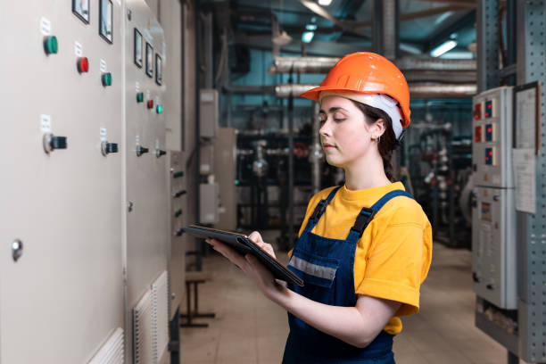 工業生産と平等の概念。タブレットを手にした制服とヘルメットをか��ぶった女性エンジニアの肖像画。背景ボイラールームで - plumber thermostat repairing engineer ストックフォトと画像