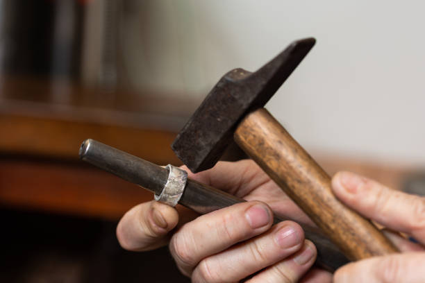 foreground, hammer hammering a silver ring to shape it in a jewelry workshop.