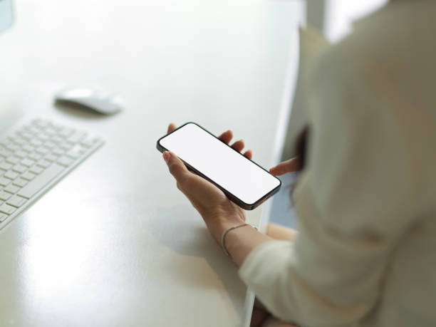 istock Female hand holding smartphone with mock up screen on computer desk 1307703931